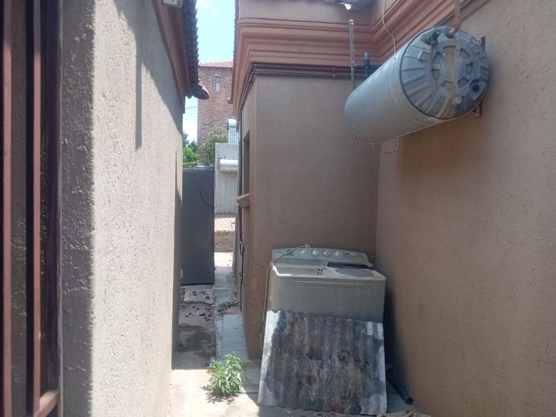 Side utility area featuring an external electric geyser and concrete paving along the building exterior.