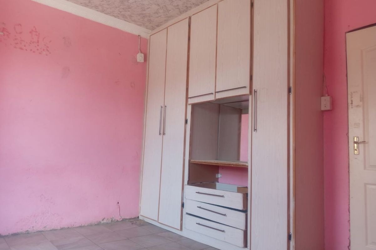 A bedroom featuring built-in wardrobes with integrated shelving and drawers, tiled flooring, and a coved ceiling, requiring cosmetic updates to the walls and cabinetry.