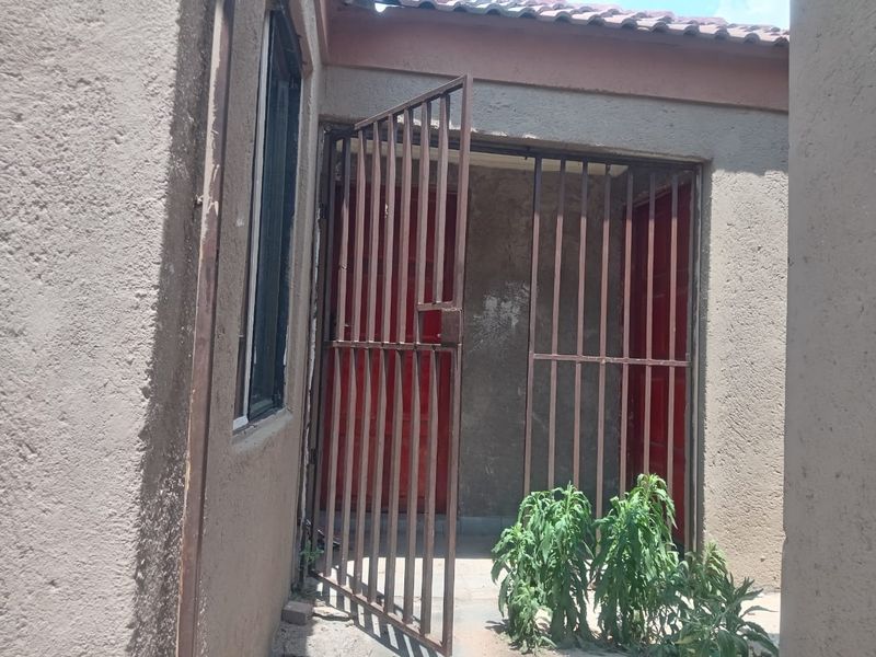 Rear exterior view showing a security gate entrance and plastered wall finish with visible surface wear.