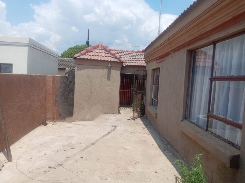 Rear exterior view of the property featuring a concrete patio area, security gate, and weathered exterior wall finishes.