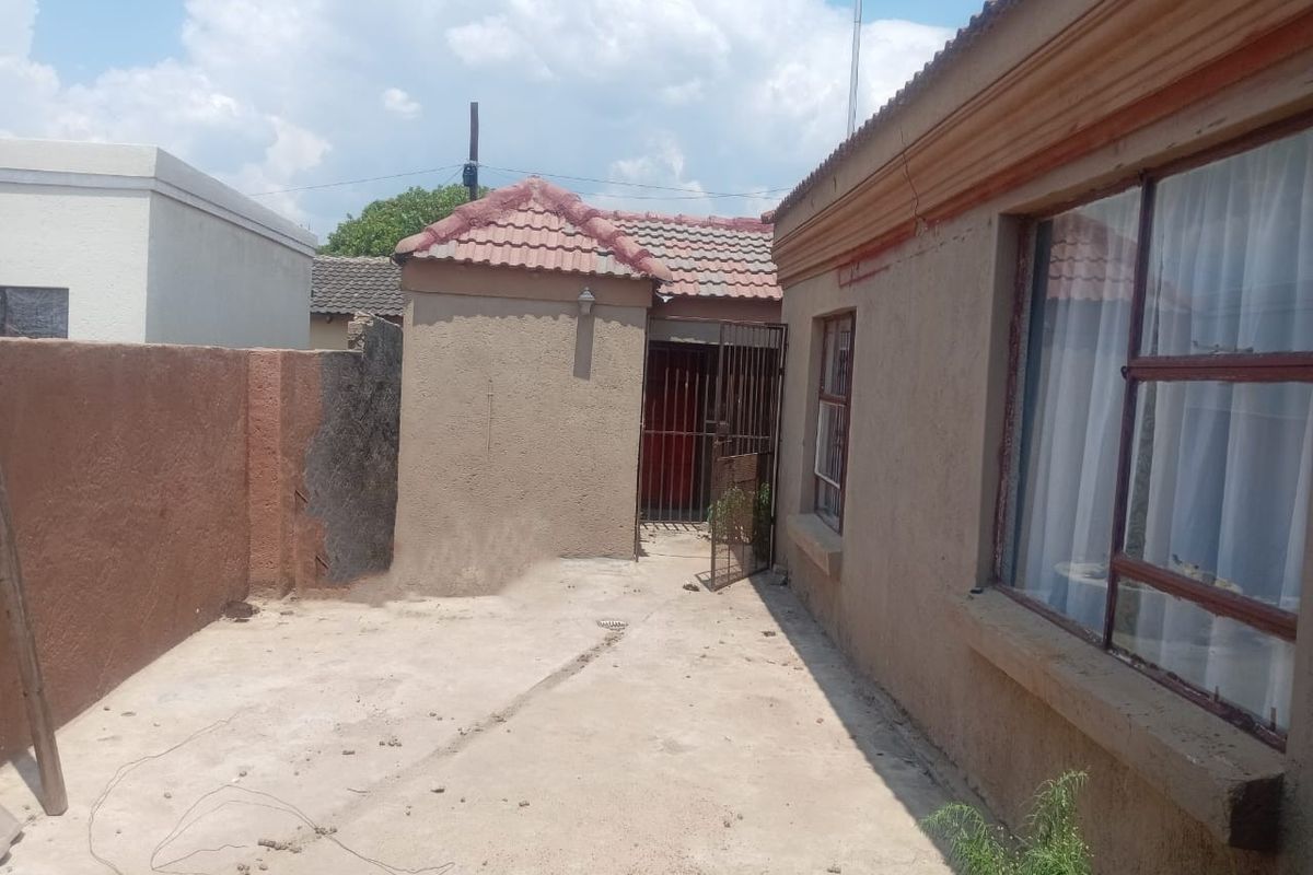 Rear exterior view of the property featuring a concrete patio area, security gate, and weathered exterior wall finishes.
