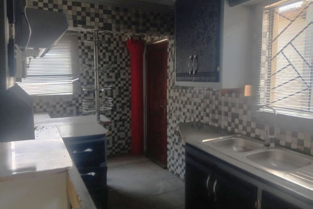 A dated kitchen featuring dark cabinetry, a double bowl sink, and a distinctive checkered tile splashback, requiring modernization to improve aesthetic appeal.