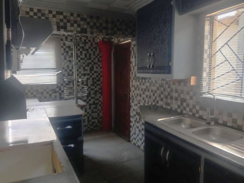 A dated kitchen featuring dark cabinetry, a double bowl sink, and a distinctive checkered tile splashback, requiring modernization to improve aesthetic appeal.