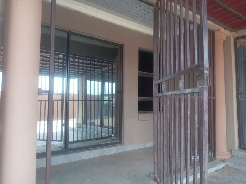 A covered patio area featuring tiled flooring, structural columns, and secure sliding glass doors with metal security gates.