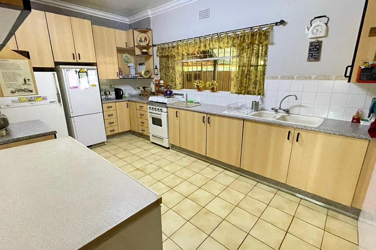A functional kitchen featuring light wood-look cabinetry, laminate countertops, a double basin sink, and a freestanding stove with tiled flooring and splashbacks.
