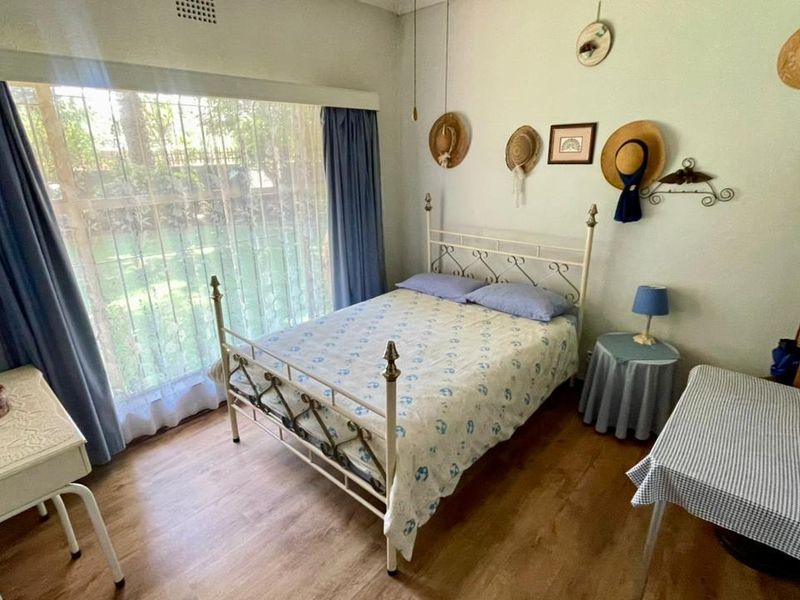 A well-lit bedroom featuring laminate flooring and a large window overlooking the garden area.