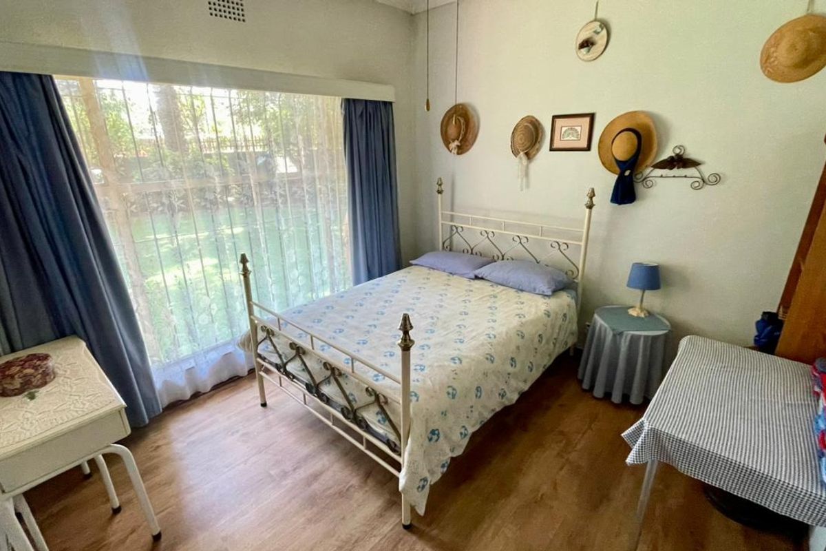 A well-lit bedroom featuring laminate flooring and a large window overlooking the garden area.