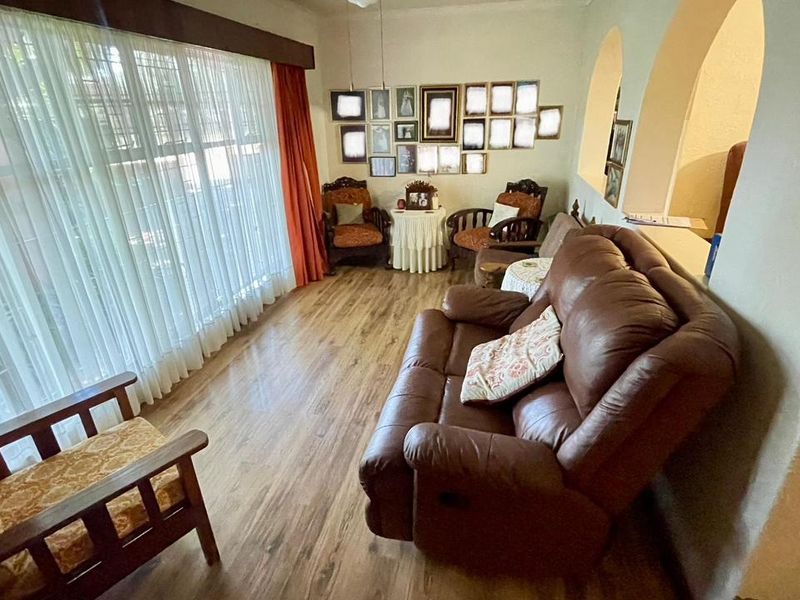 A comfortable living room featuring laminate flooring, large windows with curtains, and distinctive arched wall openings connecting to adjacent spaces.