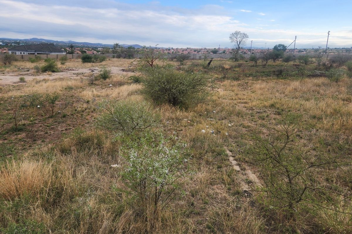 A view of a vacant residential plot featuring natural vegetation and a perimeter wall in the background.