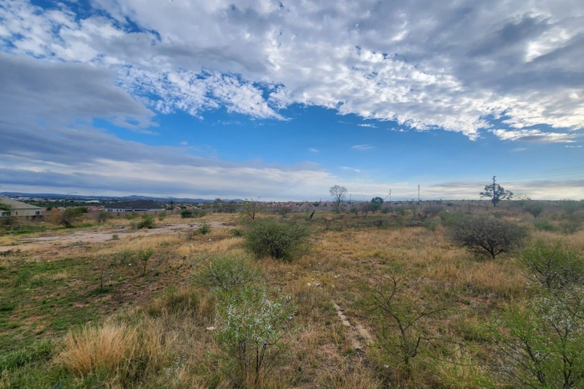A wide-angle view of an undeveloped residential plot featuring natural vegetation and open space under a clear sky.