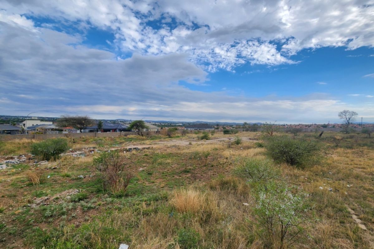 A wide-angle view of a vacant residential plot featuring natural vegetation and a perimeter wall, offering potential for future development.