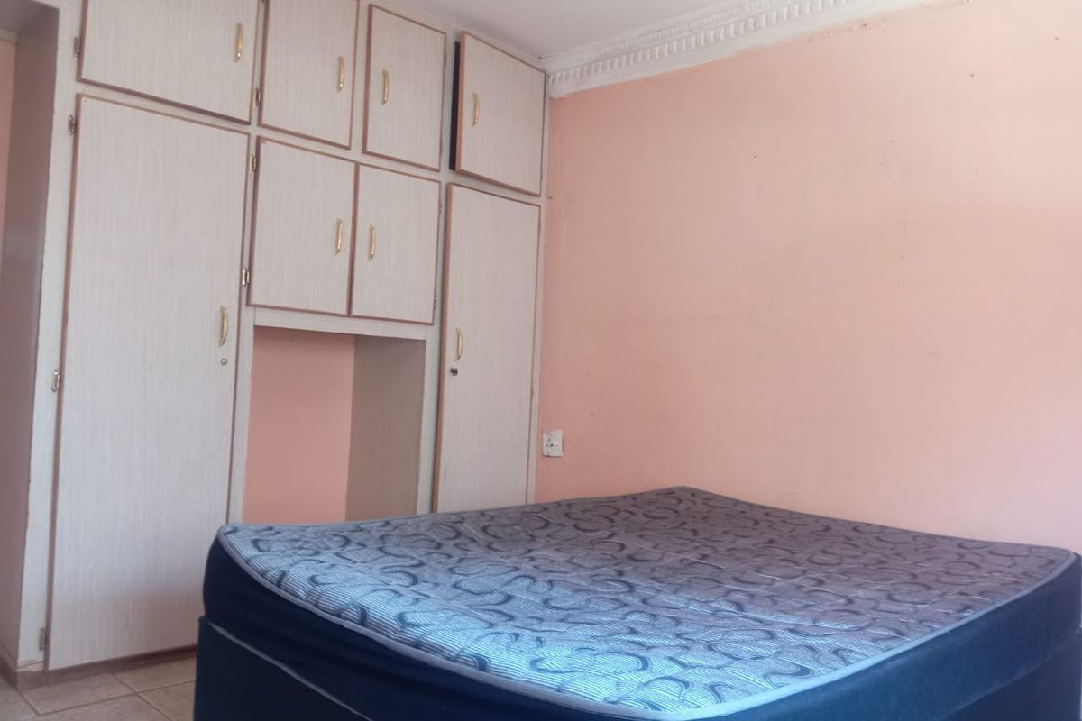 A bedroom featuring built-in cupboards, crown molding, and tiled flooring, requiring cosmetic updates to the wall finishes.