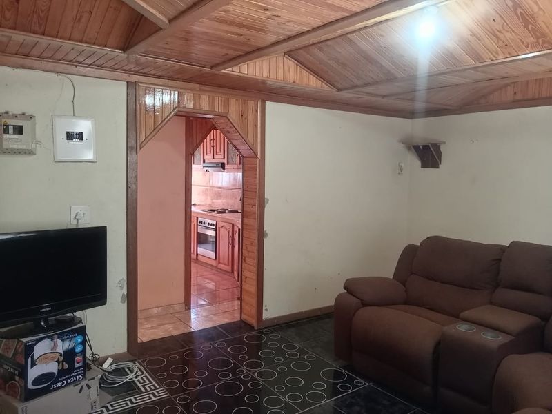 Living room featuring a timber-clad ceiling and tiled flooring, with an arched doorway leading to the kitchen area.