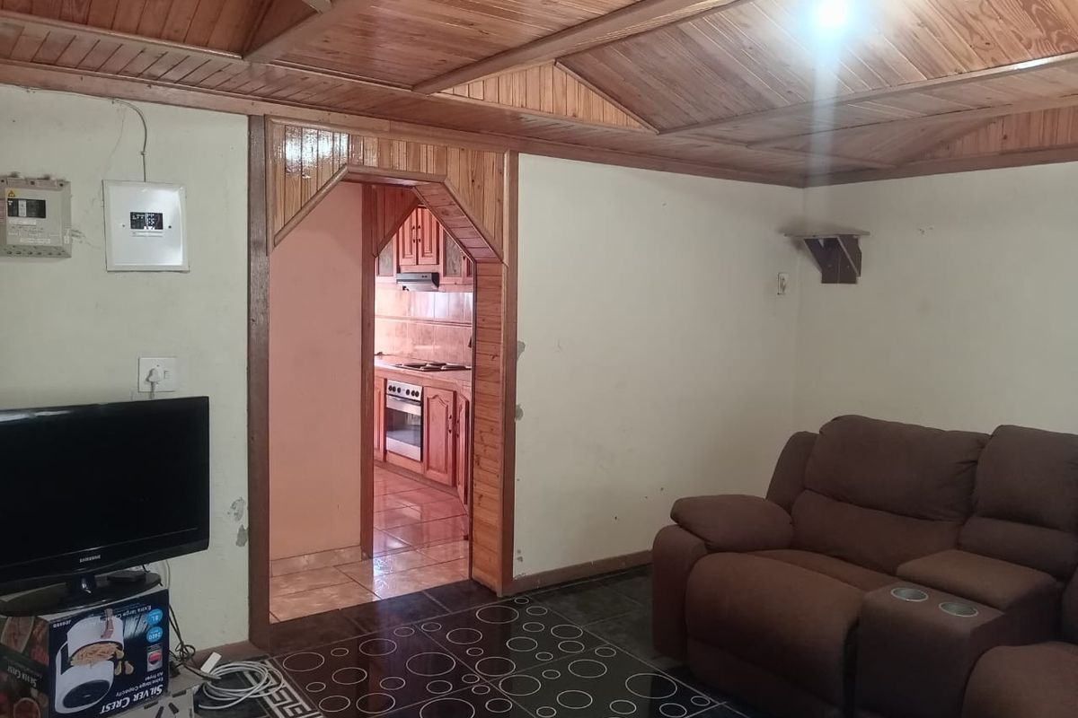 Living room featuring a timber-clad ceiling and tiled flooring, with an arched doorway leading to the kitchen area.