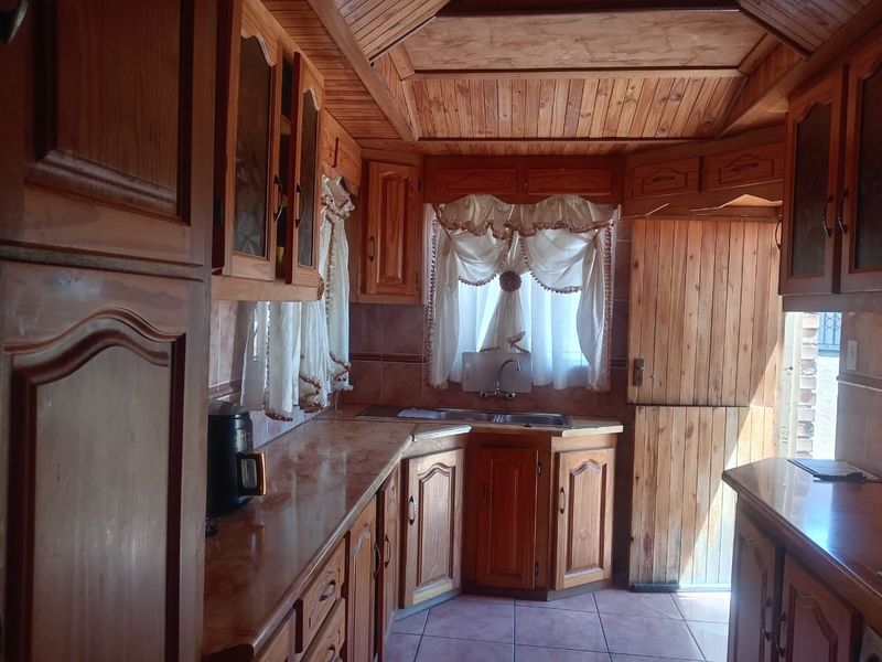 A traditional kitchen featuring extensive wooden cabinetry, tiled surfaces, and a unique wooden panelled ceiling, offering a rustic aesthetic with potential for modernization.