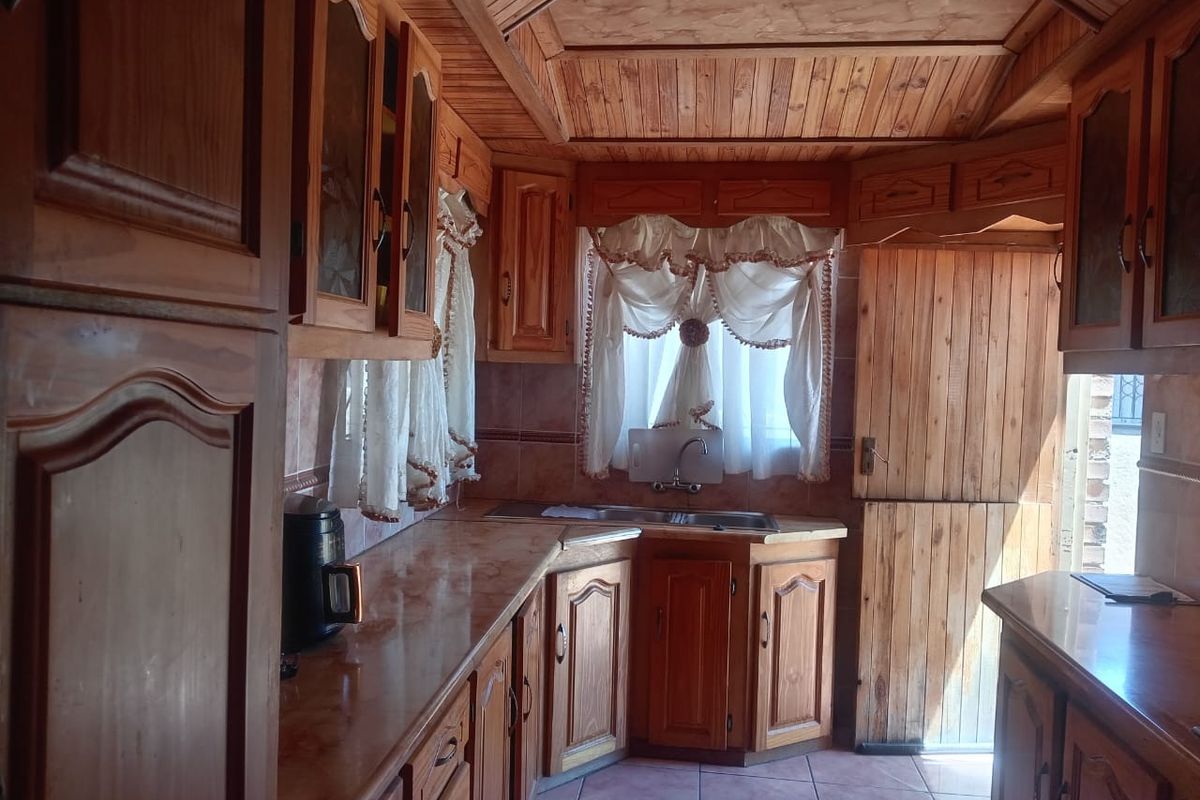 A traditional kitchen featuring extensive wooden cabinetry, tiled surfaces, and a unique wooden panelled ceiling, offering a rustic aesthetic with potential for modernization.