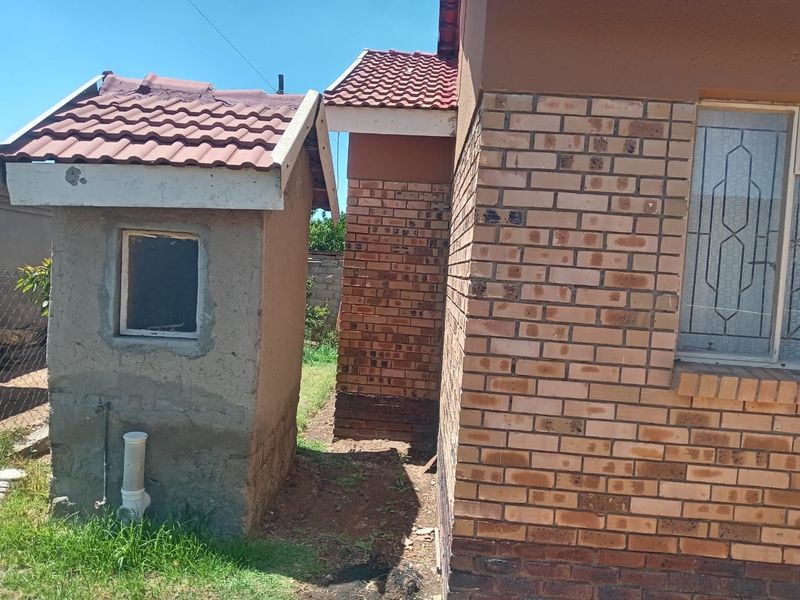 View of the rear exterior showing a face brick house wall and a separate small outbuilding with a tiled roof.