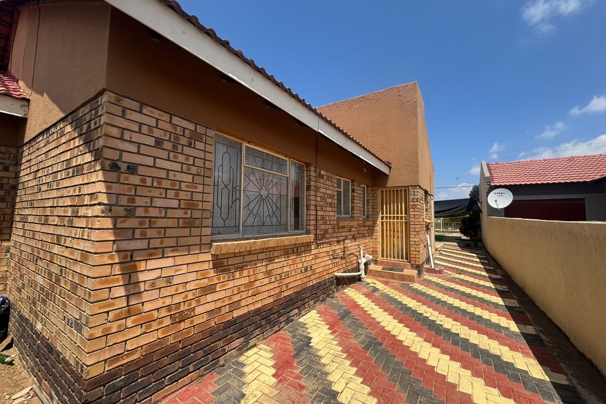 A side view of the house featuring face brick exterior walls, a security gate, and a patterned paved driveway leading to the rear area.