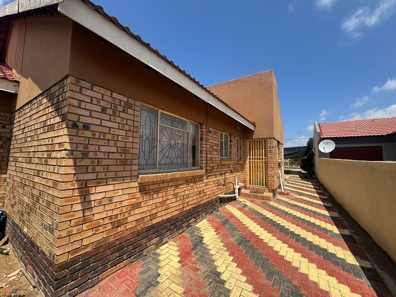 A side view of the house featuring face brick exterior walls, a security gate, and a patterned paved driveway leading to the rear area.