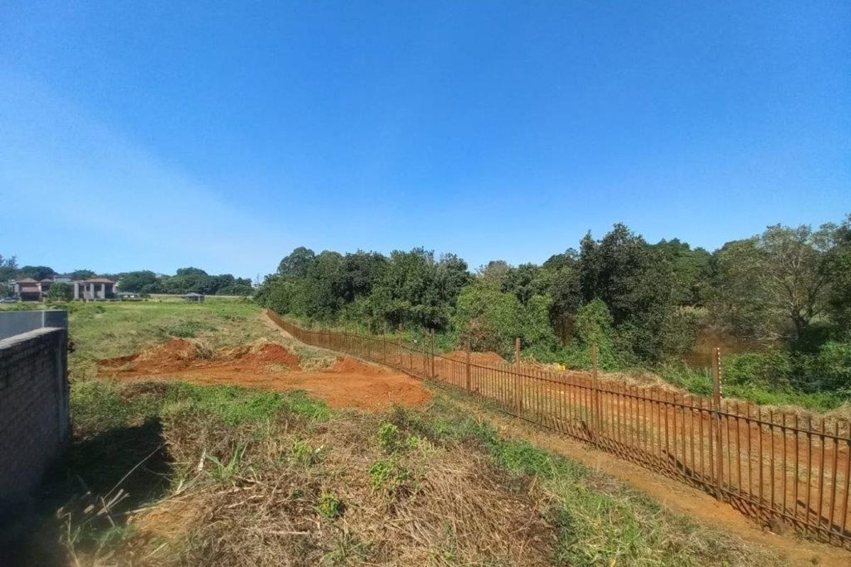 A view of the vacant residential land featuring perimeter metal fencing with electric security wires and natural vegetation.
