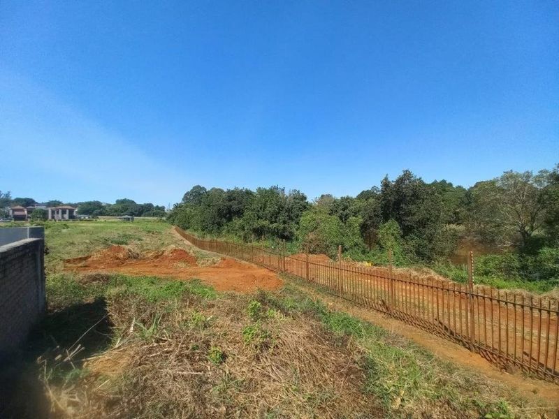 A view of the vacant residential land featuring perimeter metal fencing with electric security wires and natural vegetation.