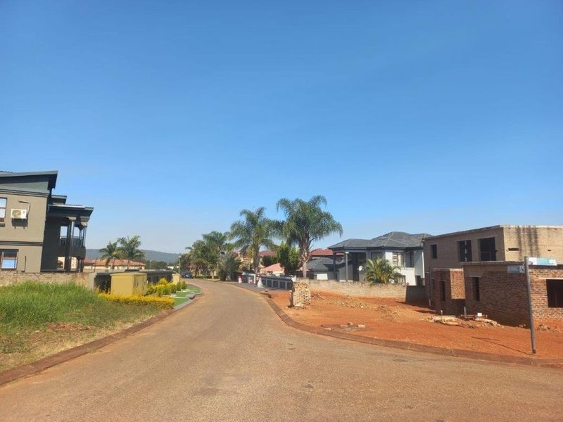 A street view of a residential neighborhood featuring paved roads, boundary walls, and surrounding residential properties under a clear blue sky.