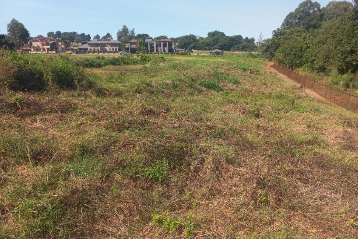 A view of a vacant residential plot featuring natural vegetation and perimeter fencing, situated in a developed neighborhood.