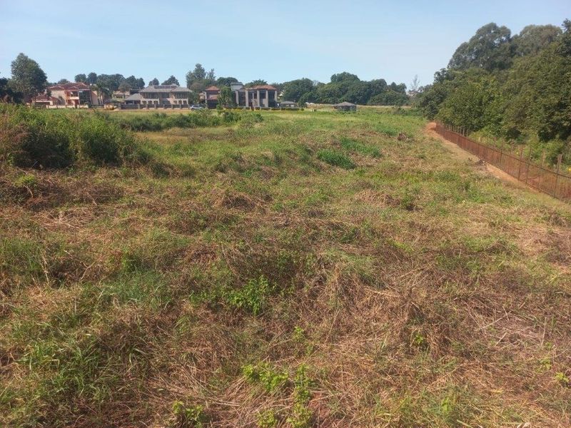 A view of a vacant residential plot featuring natural vegetation and perimeter fencing, situated in a developed neighborhood.