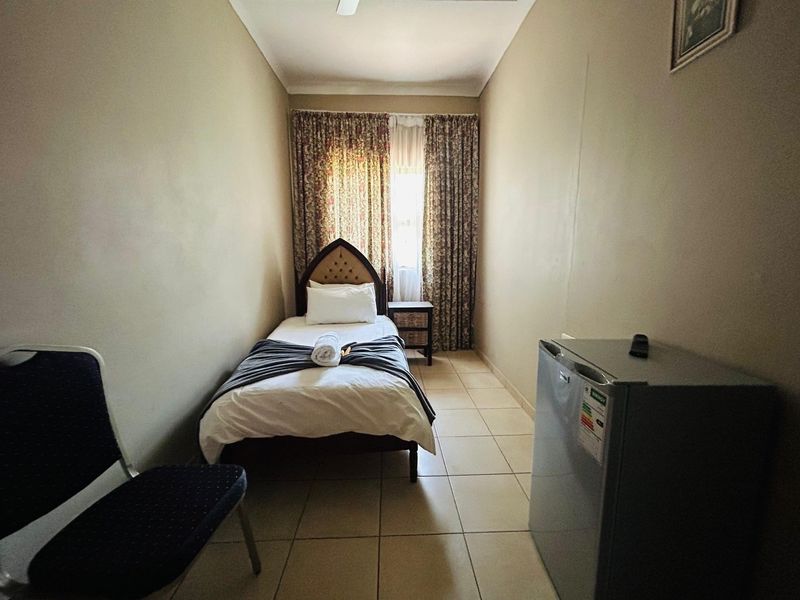 A compact bedroom featuring tiled flooring and a ceiling fan, providing a functional and straightforward living space.