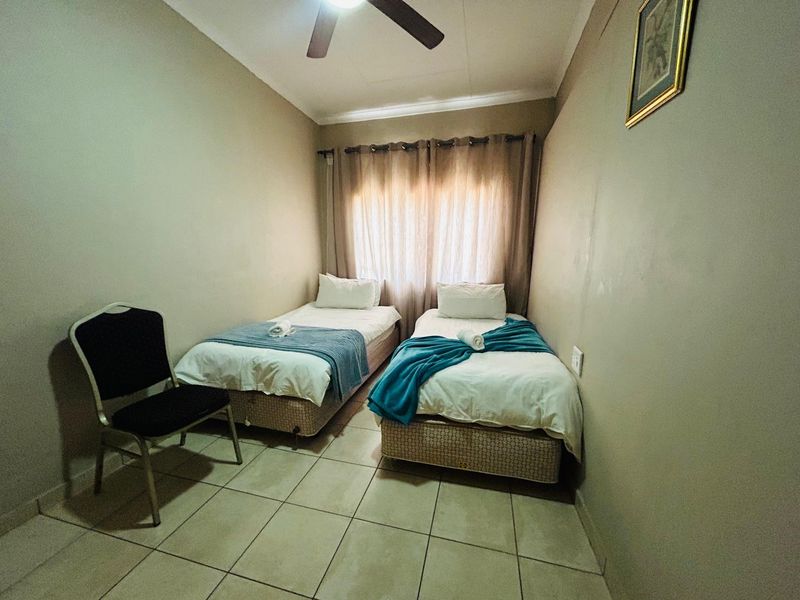A functional bedroom featuring tiled flooring, a ceiling fan, and window treatments, providing a simple and practical sleeping space.