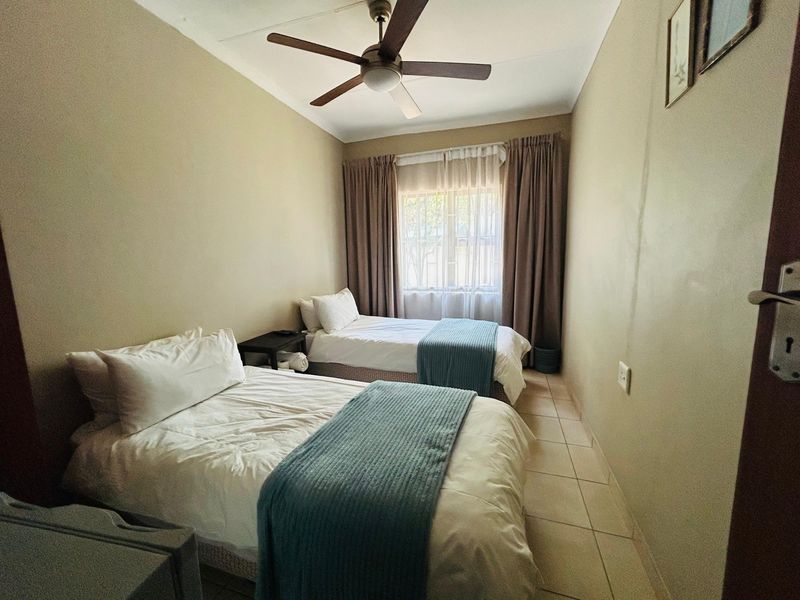 A functional bedroom featuring tiled flooring, a ceiling fan, and window treatments, providing a comfortable space for rest.