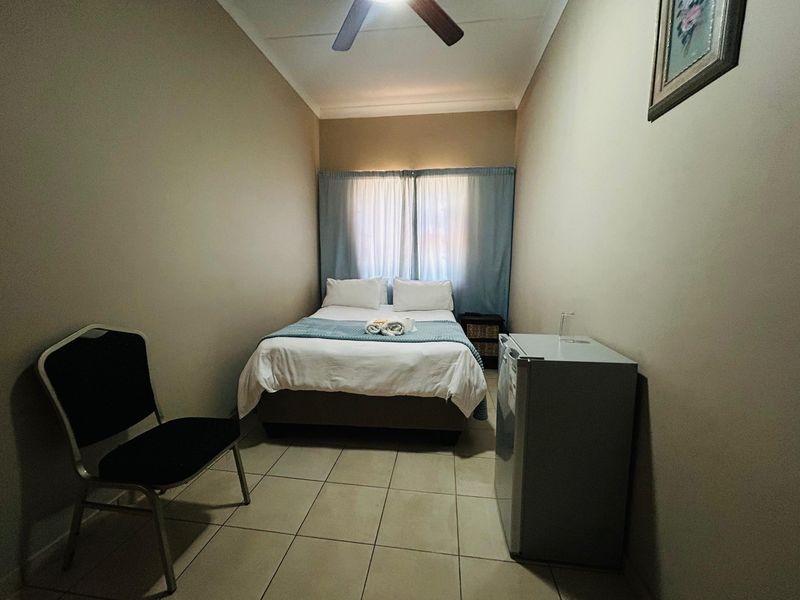 A compact bedroom featuring tiled flooring and a ceiling fan, providing a functional and simple living space.