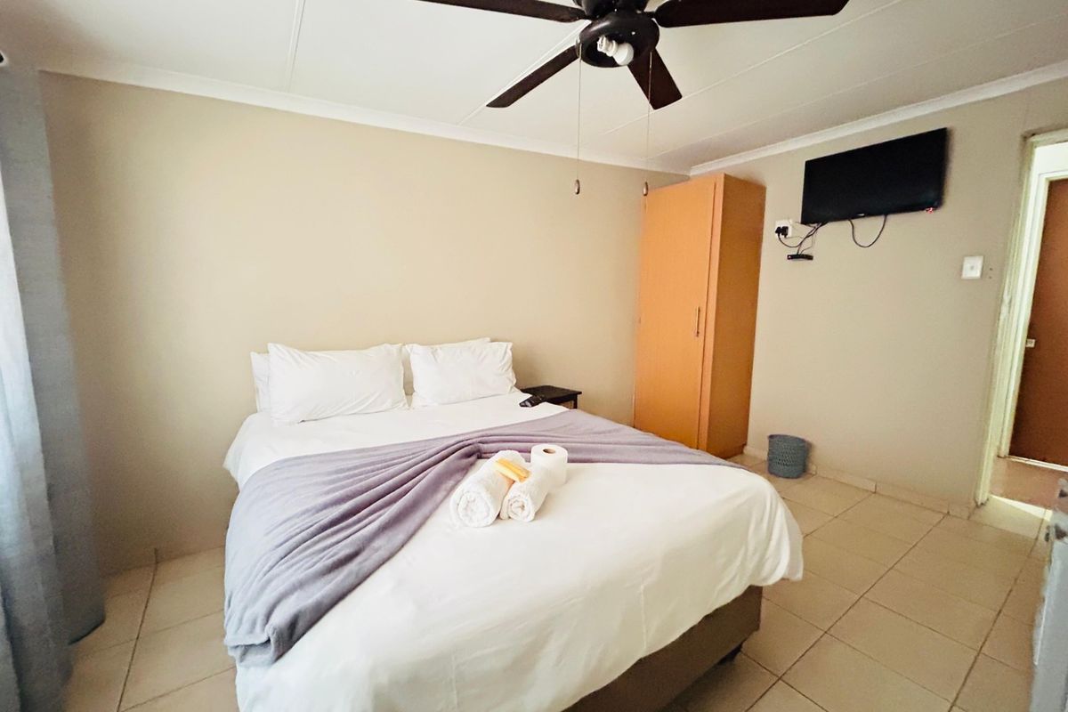 A functional bedroom featuring tiled flooring, a ceiling fan, and a built-in wardrobe, offering a simple and practical living space.