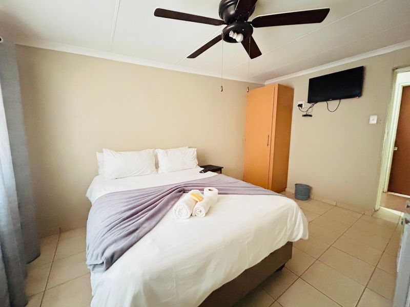 A functional bedroom featuring tiled flooring, a ceiling fan, and a built-in wardrobe, offering a simple and practical living space.