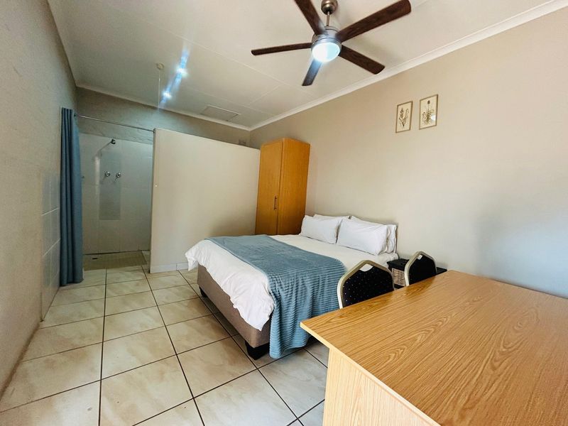 A bedroom featuring tiled flooring, a ceiling fan, and an integrated open-plan shower area.