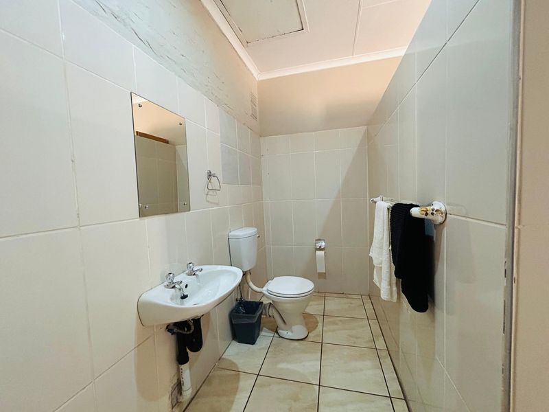 A functional bathroom featuring ceramic wall and floor tiles, a wall-mounted basin, and a standard toilet, requiring minor cosmetic updates.