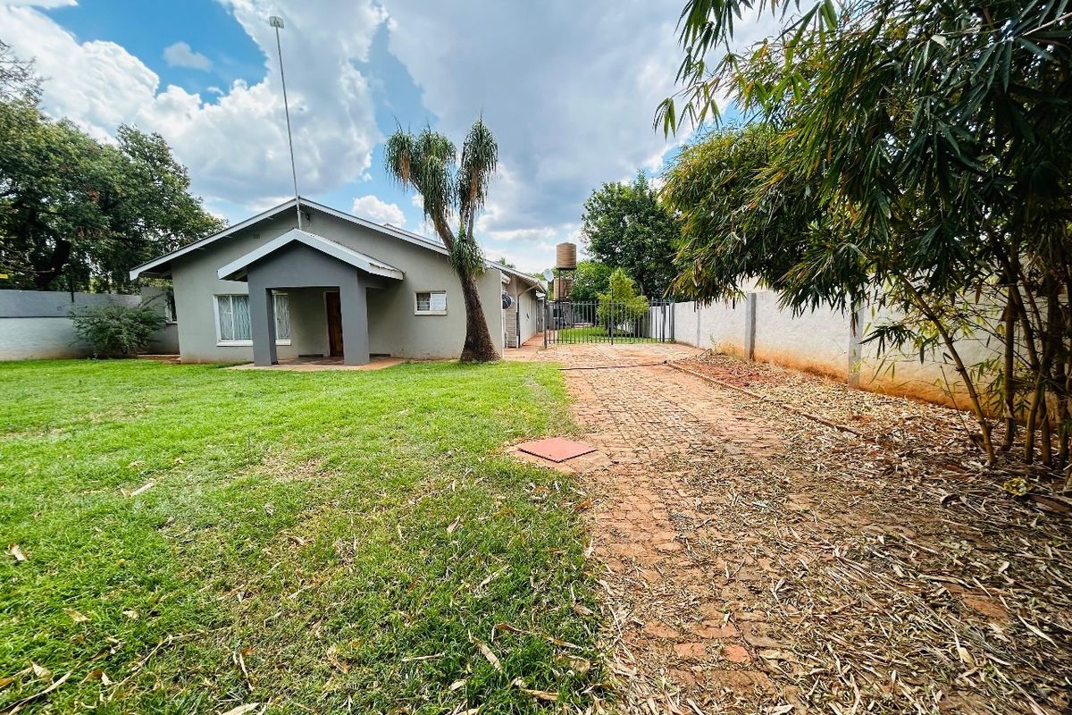 Rear view of the property featuring a paved driveway, lawn area, perimeter walling, and a water tank.