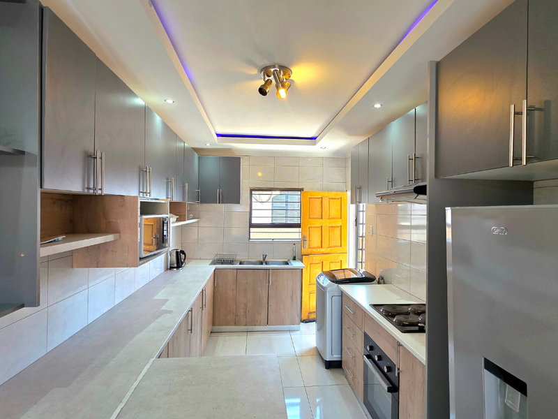 Modern kitchen featuring two-tone cabinetry, stone-look countertops, built-in oven and hob, and integrated lighting, providing a functional and contemporary workspace.