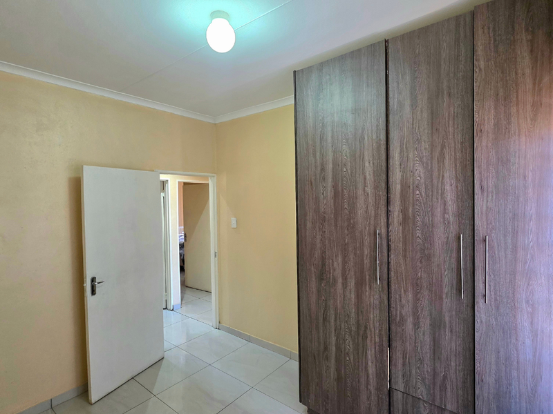 A clean, empty bedroom featuring neutral walls, modern tiled flooring, and spacious built-in wooden cupboards.