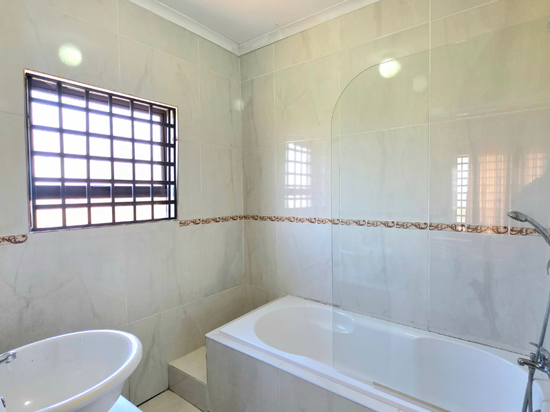 A clean, tiled bathroom featuring a built-in bathtub with a glass shower screen, handheld shower head, and a pedestal basin.