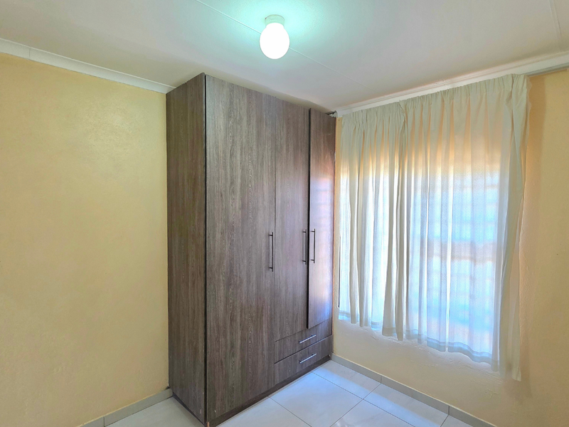 A bright bedroom featuring neutral walls, tiled flooring, and a large built-in wooden wardrobe with ample storage space.