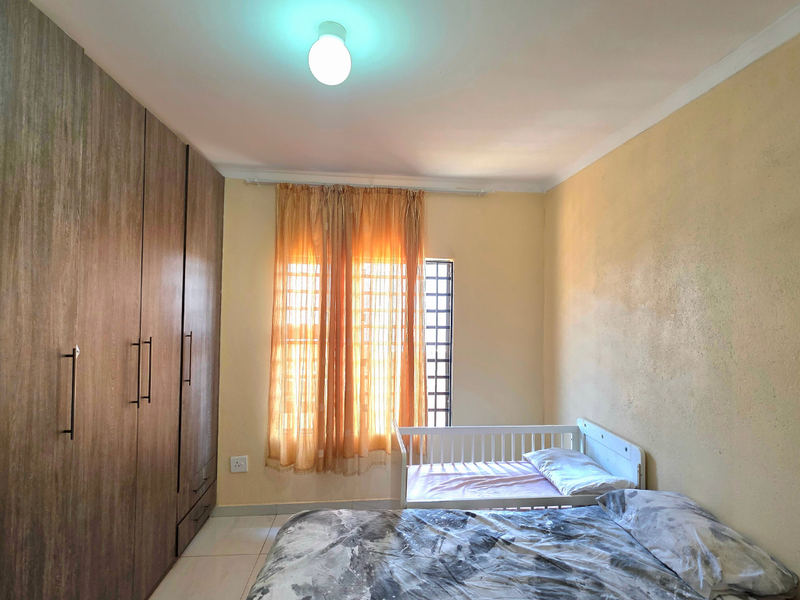 A bedroom featuring built-in wooden wardrobes, tiled flooring, and security bars on the window.