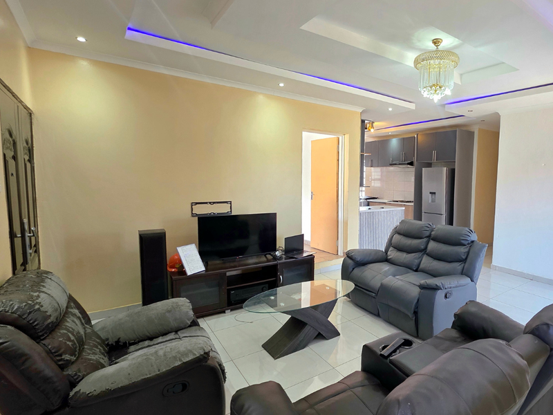 Open-plan living area featuring tiled floors, recessed ceiling lighting with accent strips, and a connected kitchen with modern cabinetry and island.