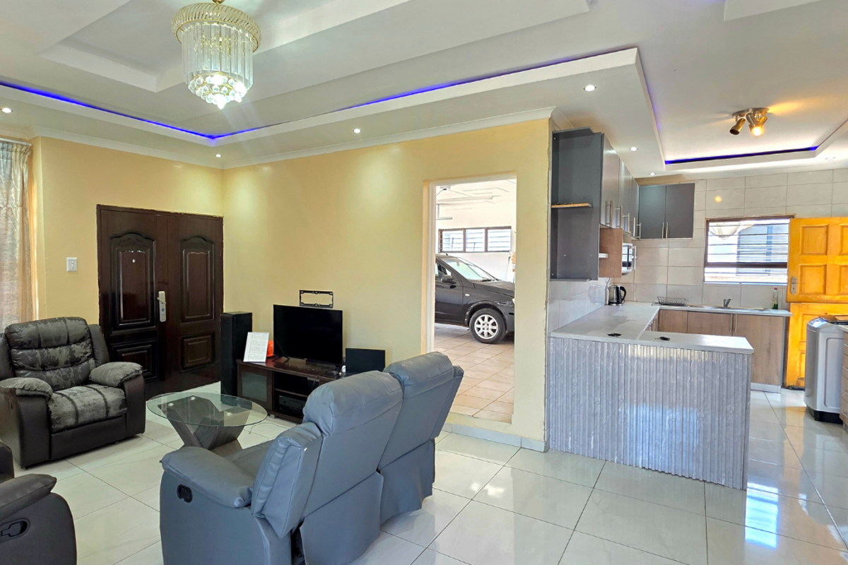 Open-plan living and kitchen area featuring porcelain floor tiles, recessed ceiling lighting with LED accents, and a functional kitchen layout with breakfast bar.