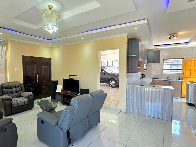 Open-plan living and kitchen area featuring porcelain floor tiles, recessed ceiling lighting with LED accents, and a functional kitchen layout with breakfast bar.