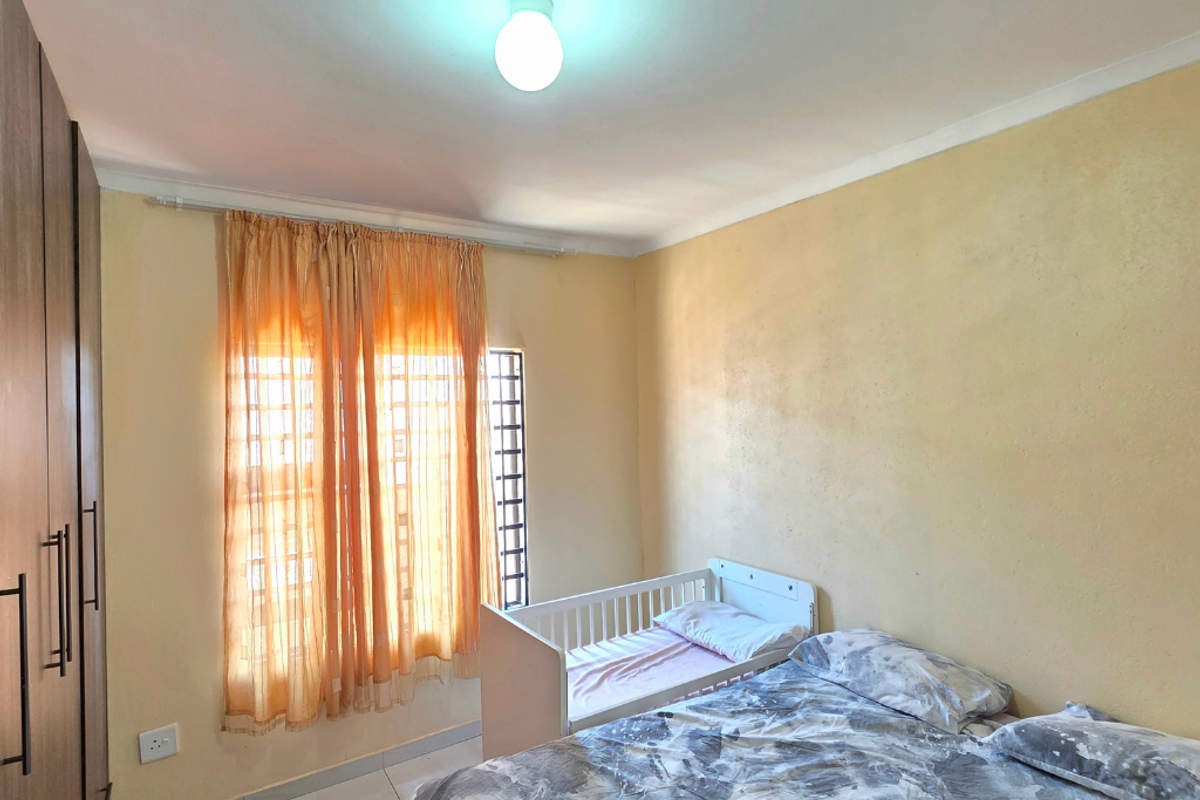 A functional bedroom featuring built-in cupboards, tiled flooring, and security bars on the window, providing a practical and secure living space.