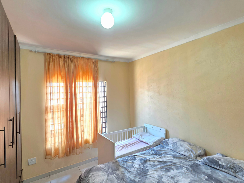 A functional bedroom featuring built-in cupboards, tiled flooring, and security bars on the window, providing a practical and secure living space.