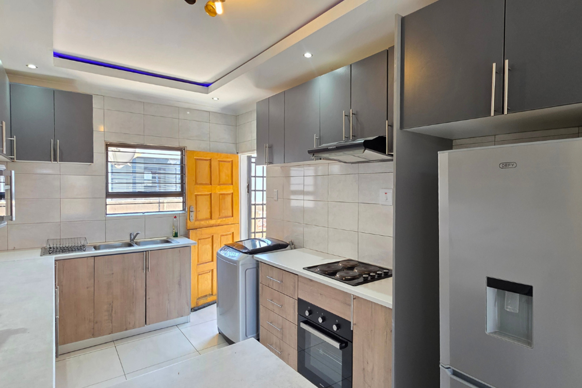 Modern kitchen featuring two-tone cabinetry, built-in oven and hob, extractor fan, double sink, and tiled backsplash with recessed and cove lighting.