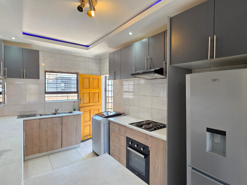 Modern kitchen featuring two-tone cabinetry, built-in oven and hob, extractor fan, double sink, and tiled backsplash with recessed and cove lighting.