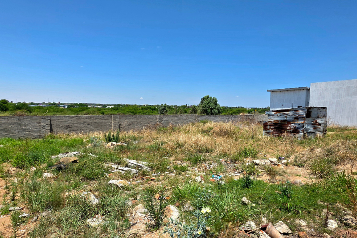 Vacant residential land featuring a perimeter brick wall and a small, weathered corrugated metal structure on the property.